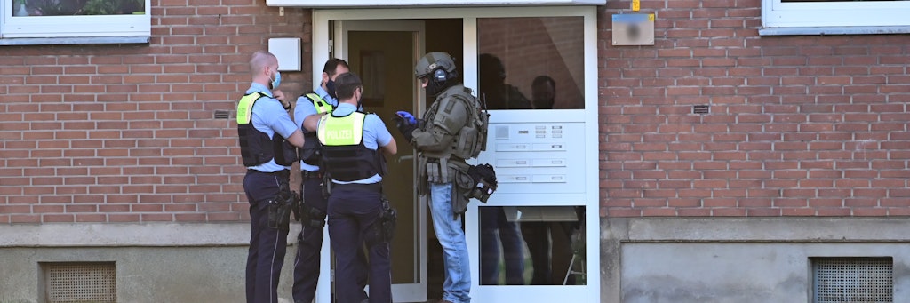 Polizei und ein SEK-Beamter stehen vor der Eingangstür des Mehrfamilienhauses in Krefeld. 