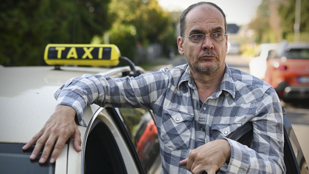 Taxifahrer Stephan Fiedler vor seinem Taxi, das während seiner Kurzarbeit stillgelegt werden musste. Er ärgert sich, dass sein Chef für seinen Verdienstausfall geradestehen muss.