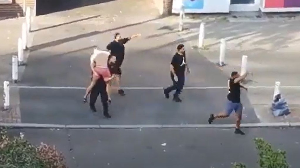 Ersthelfer, Angestellte eines Friseur-Salons, tragen das schwer verletzte Opfer zu einer Polizeistreife, die gerade am Tatort eintrifft. Das Bild stammt aus einem Zeugenvideo, was von dem Haus gegenüber aufgenommen wurde. 