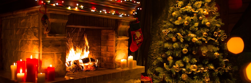 Neben einem geschmückten Tannenbaum brennt ein Feuer im Kamin.