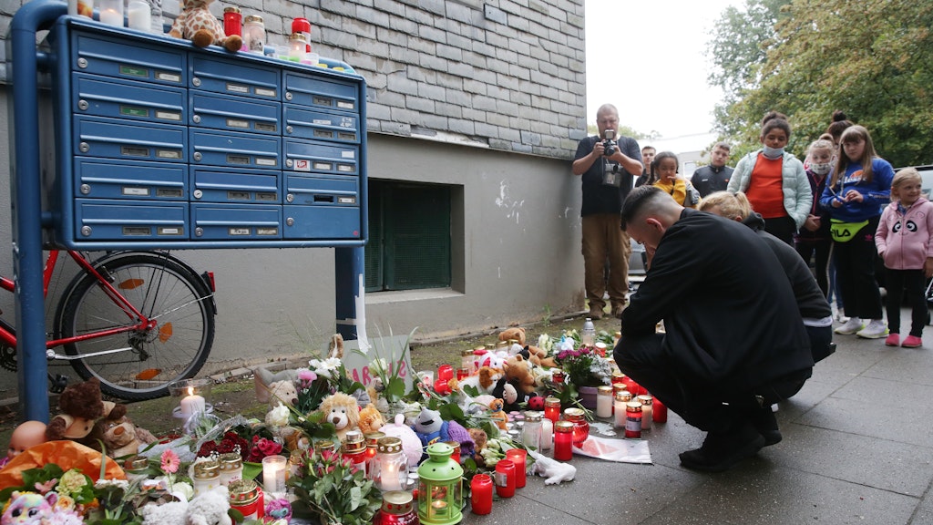 Trauende knien vor Blumen, Kerzen und Stofftieren. 