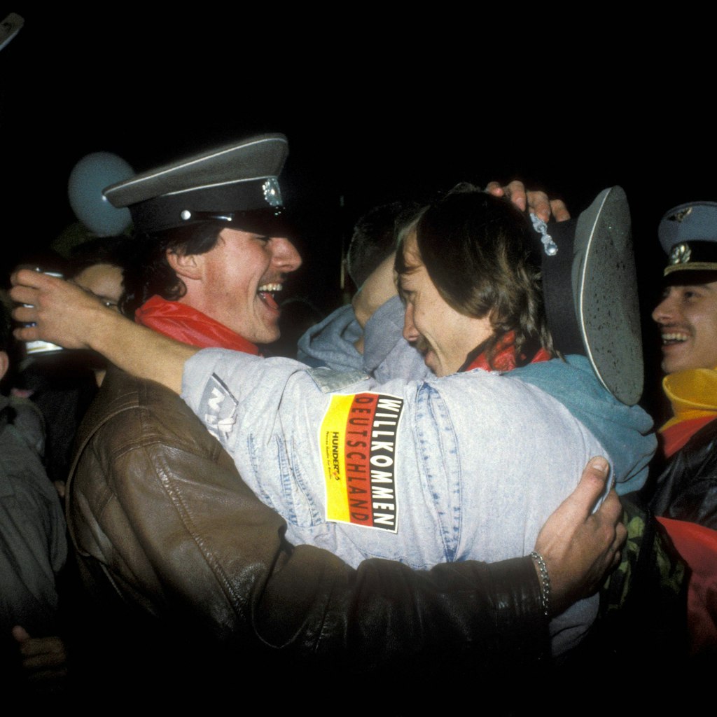 Feiernde Männer mit NVA-Mützen umarmen sich am 3. Oktober 1990, dem Tag der Wiedervereinigung.