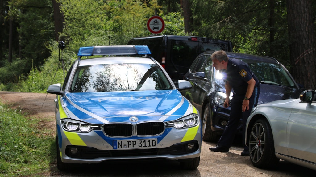 Ein Polizist steht auf einem Waldweg an einem Einsatzfahrzeug der Polizei. Ein Pilzsammler hat in einem Wald im Landkreis Nürnberger Land einen toten Mann gefunden.