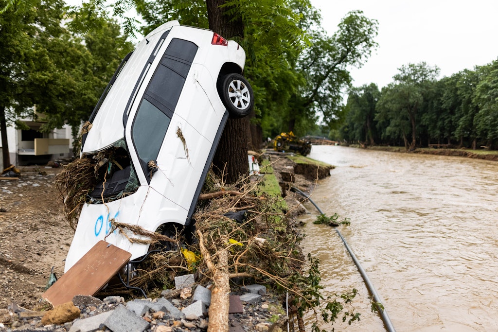 Ein vom Hochwasser angeschwemmtes Auto lehnt an einem Baum in Bad Neuenahr während im Hintergrund der Fluss Ahr zu sehen ist.