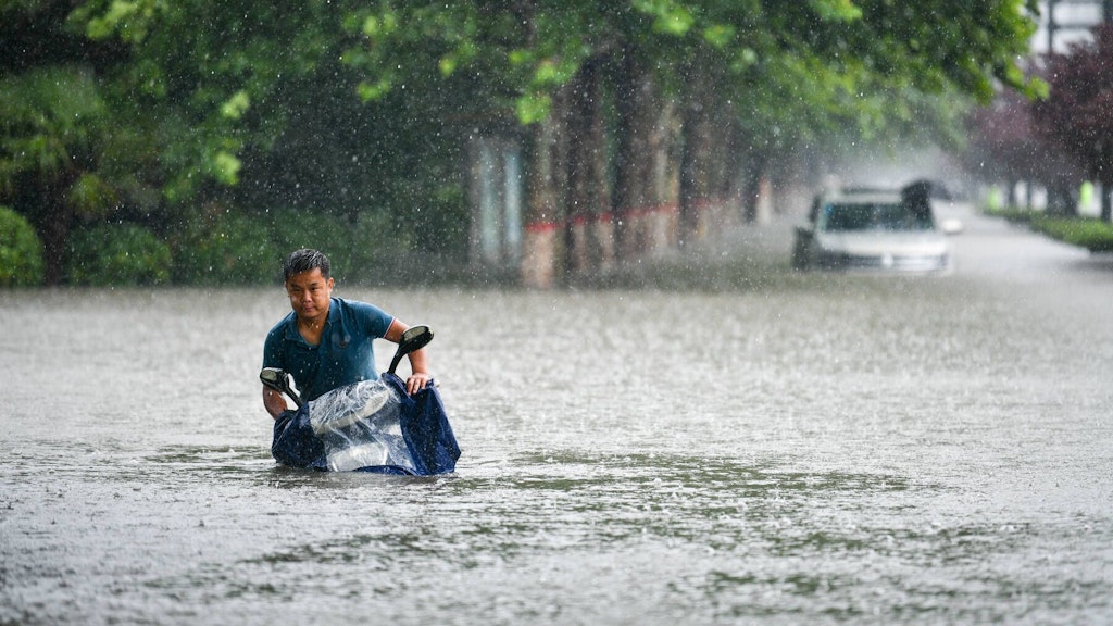 Ein Mann mit einem Moped kann sich in den Wassermassen auf einer Straße in Zhengzhou nur schwer auf den Beinen halten. 