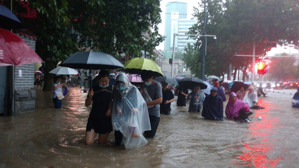 Menschen waten in der zentralchinesischen Provinz Henan durch eine überflutete Straße. 