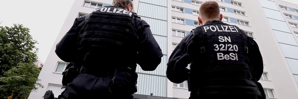  Zwei Polizisten stehen vor einem Hochhaus. 800 Polizisten haben in Sachsen und Brandenburg Wohnungen von Tatverdächtigen der schweren Fußball-Krawalle bei Dynamo Dresden durchsucht.
