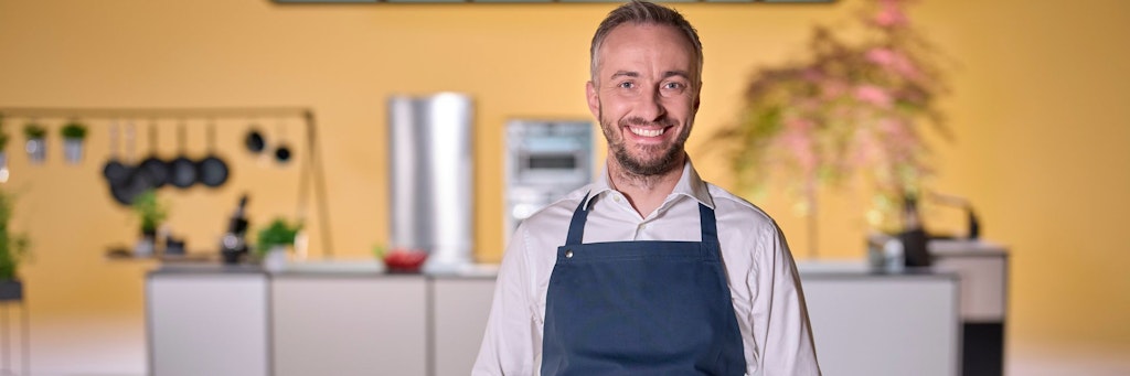 Moderator Jan Böhmermann steht in der Küche von „Böhmi brutzelt“, seiner Kochsendung bei ZDFneo, in der er mit wechselnden Gästen Essen zubereitet und plaudert. 