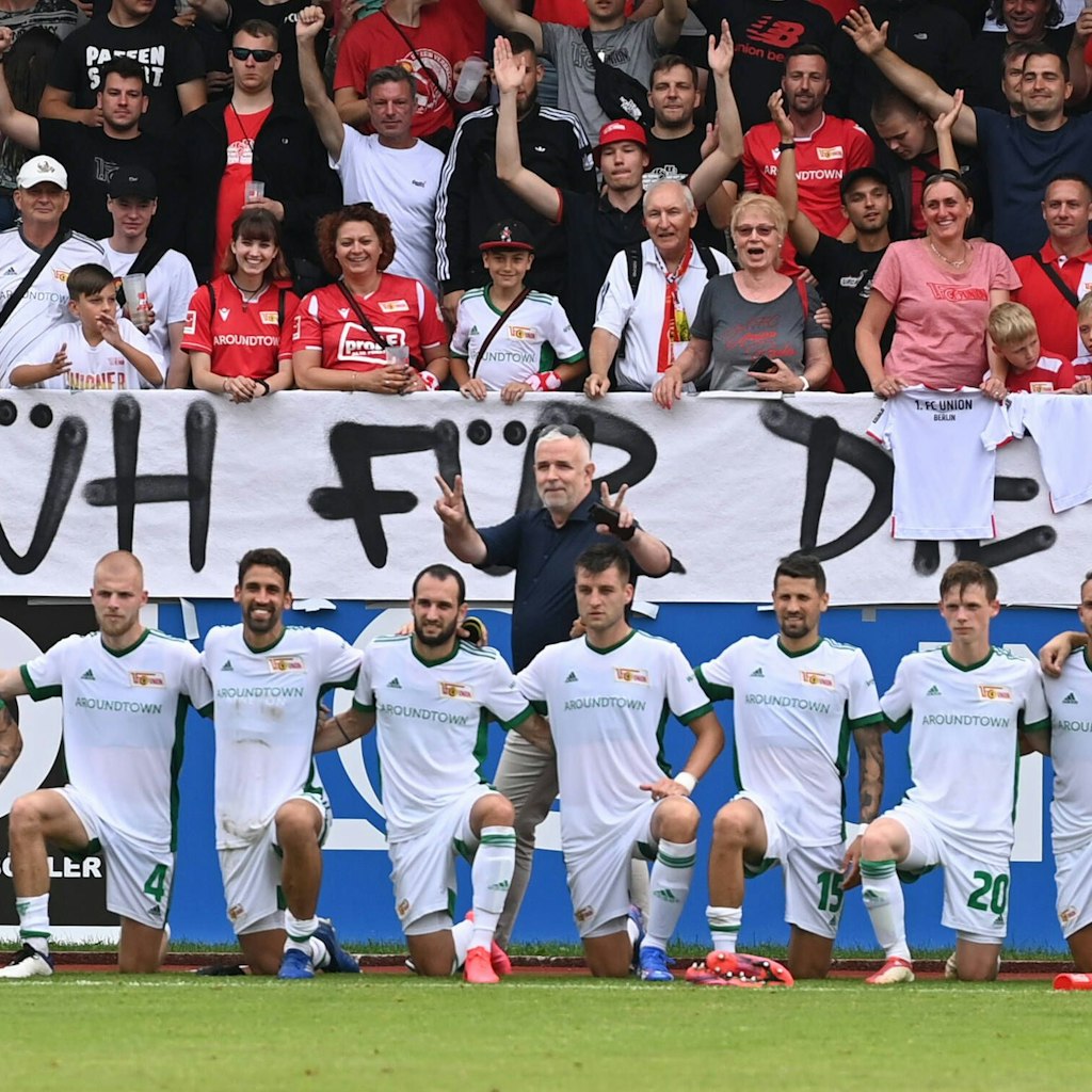 Dirk Zingler macht hinter der Mannschaft stehend das Victory-Zeichen.
