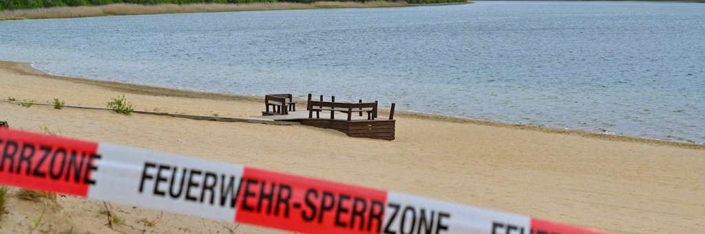 Mit einem Flatterband ist ein Zugang zum Strand des Helenesees abgesperrt. Die Hoffnung vieler Badegäste, der Stadt und des Pächters hat sich zerschlagen: Der Helenesee bei Frankfurt (Oder) bleibt aus Sicherheitsgründen weiter gesperrt.