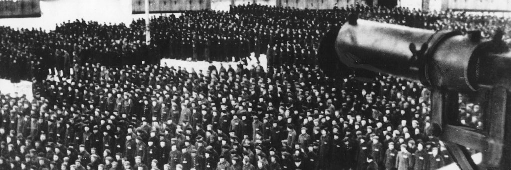 Häftlinge sind im KZ Sachsenhausen angetreten, ein Maschinengewehr ist auf sie gerichtet. Ein jetzt 100 Jahre alter Mann war in dem Lager, in dem mehrere 10.000 Menschen ihr Leben ließen, Wachmann. 