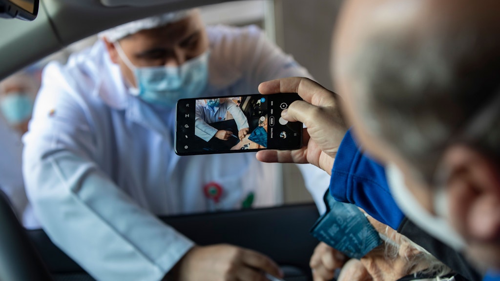 Ein Mann in Sao Paulo in Brasilien fotografiert mit dem Handy, wie seiner Mutter im Auto eine Covid-19-Impfung verabreicht wird. 