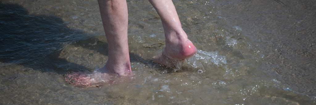 Ein Mann watet durch das flache Wasser am Strand des Seebads. Viele Ostseebäder machen derzeit mit Aushängen auf die Gefahr durch Vibrionen aufmerksam. 