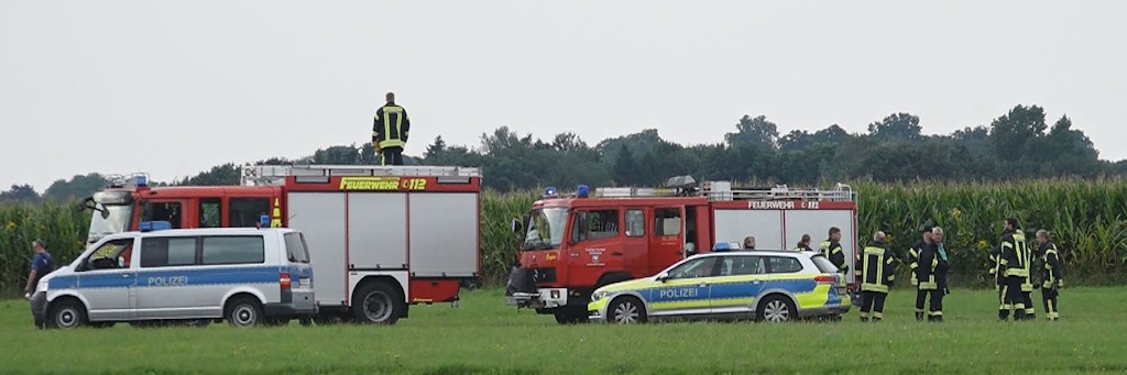 Feuerwehrleute und Polizisten stehen am Rande des Maisfeldes in Ganderkesee, in dem der tödlich abgestürzte Fallschirmspringer gefunden wurde. 