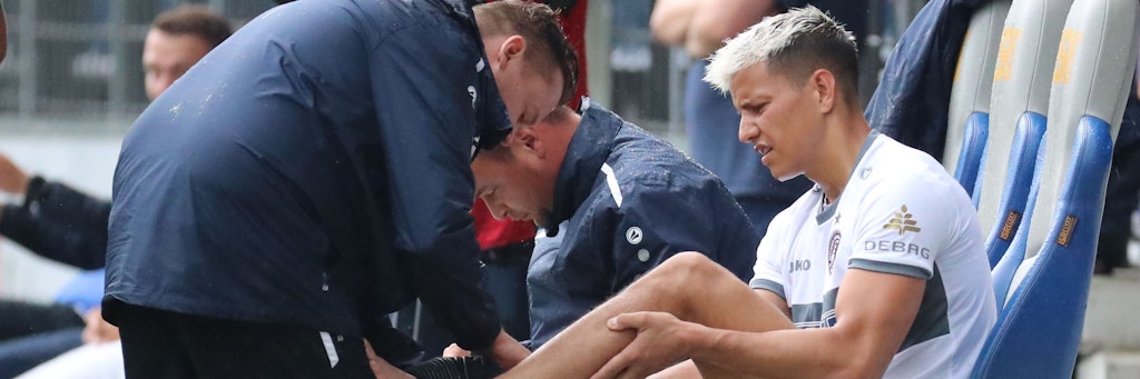 Philip Schulz erträgt tapfer, dass Dynamo-Physio Adrian Marklowski den verletzten Knöchel mit einem Verband stabilisiert.