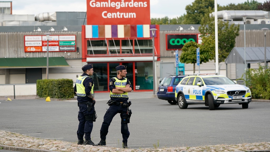Zwei Polizisten stehen am Tatort nach mutmaßlichen Schüssen im Stadtteil Nasby auf einem Parkplatz.