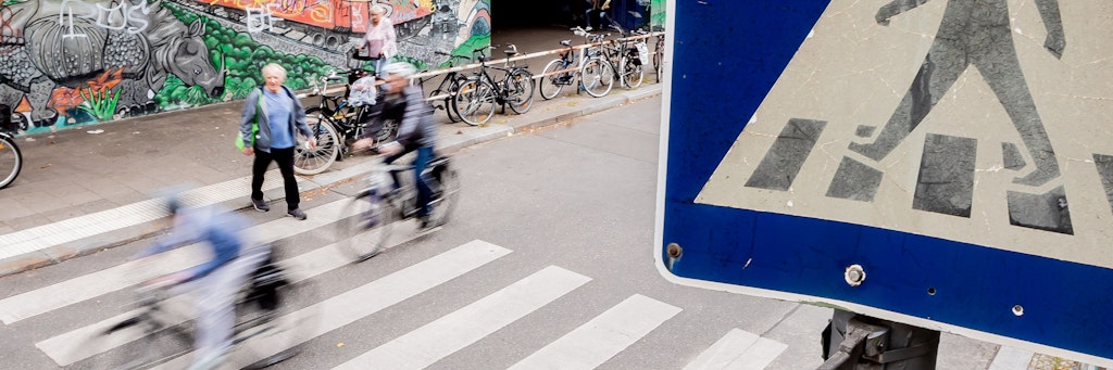 Fahrradfahrer und ein Fußgänger überqueren einen Zebrastreifen am S-Bahnhof Friedenau.