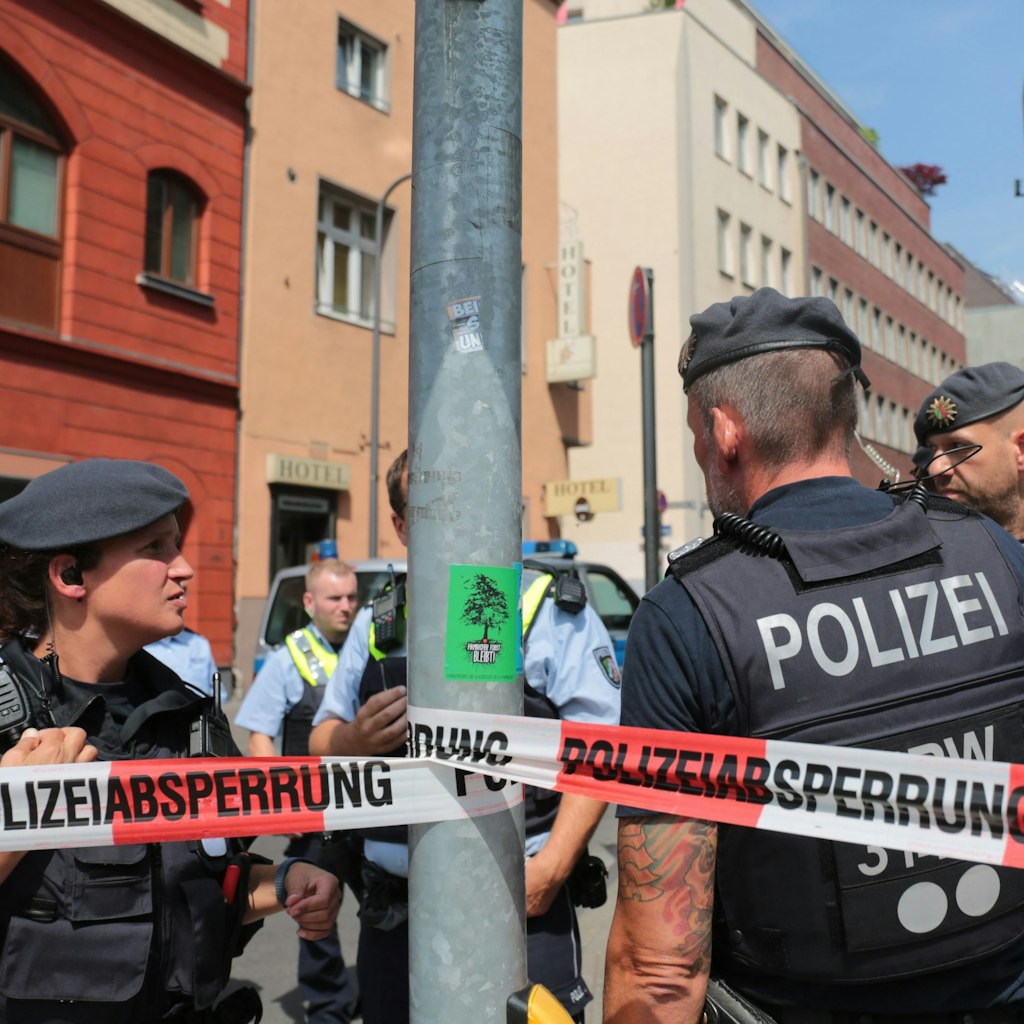 Polizisten stehen vor einem Wohngebäude in der Kölner Innenstadt hinter einem Absperrband. Die Polizei hatte im Juli 2019 Wohnungen mutmaßlicher Gefährder aus dem islamistischen Umfeld unter anderem in Köln durchsucht.