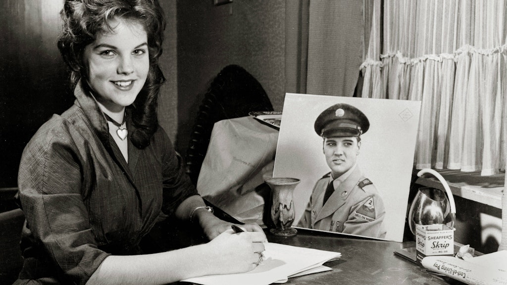 Die 16-jährige Priscilla sitzt neben einem Bild von Elvis in Militäruniform.