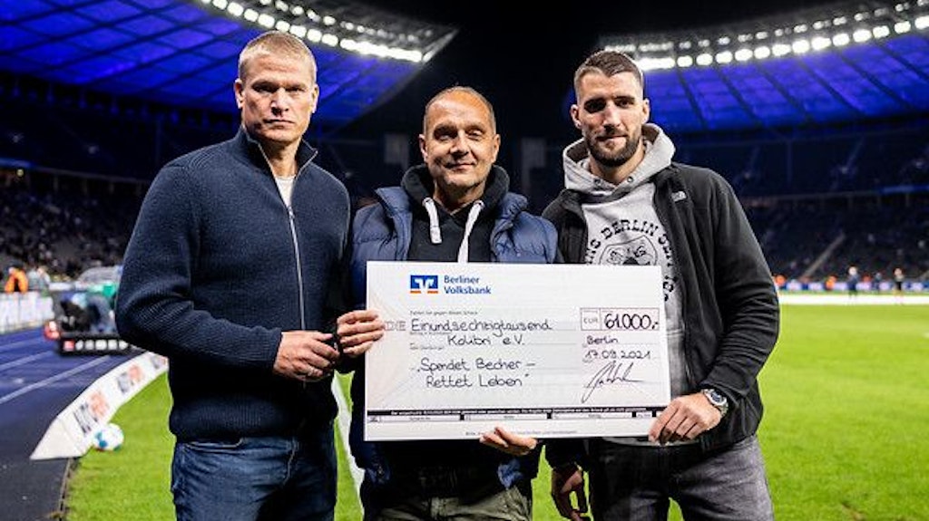 Paul Keuter, Mitglied der Geschäftsleitung von Hertha, und einen der Initiatoren von Harlekins Berlin 98, überreichen Kolibri-Mitarbeiter Andreas Landgraf den symbolischen Scheck.