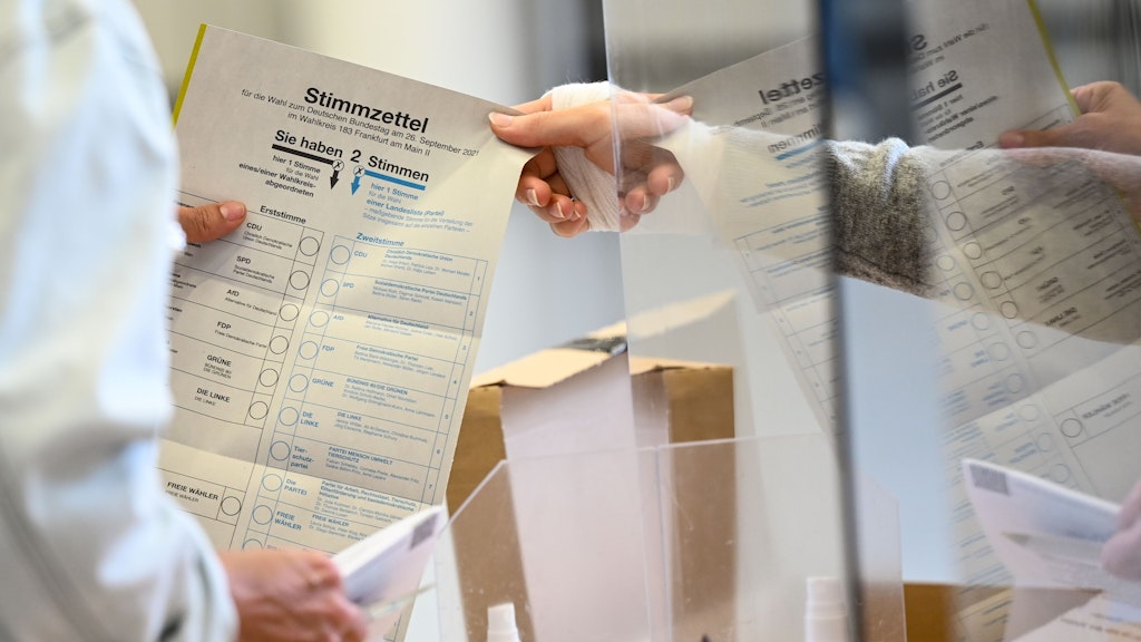 Eine Wahlhelferin überreicht einer Frau im Wahllokal ihren Stimmzettel für die Bundestagswahl 2021. 