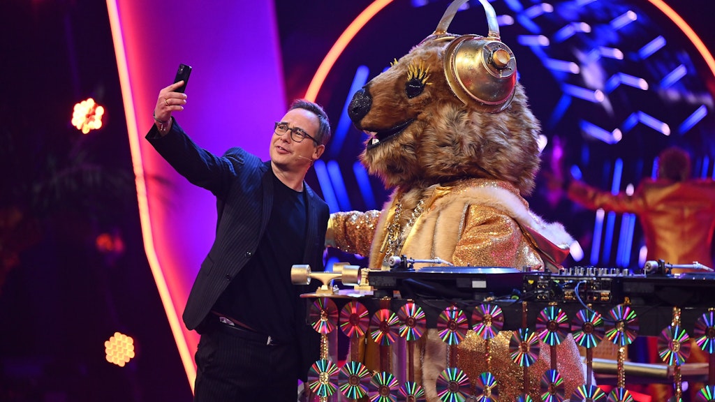 Moderator Matthias Opdenhövel macht auf der „Masked Singer“-Bühne ein Selfie mit der Figur Quokka aus Staffel vier.