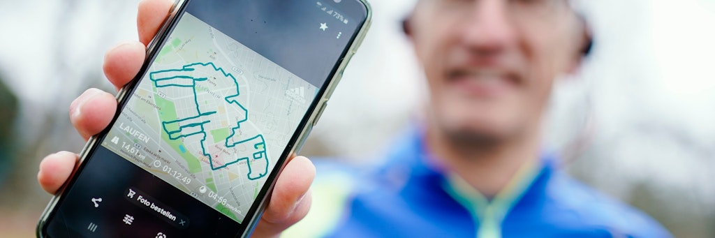 Norbert Asprion hält im Ebertpark sein Mobiltelefon mit dem Bild einer von ihm gelaufenen Wegstrecke in Form eines Kamels in den Händen. 