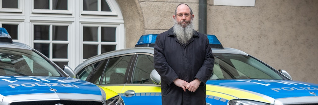 Rabbiner Shneur Trebnik steht im Ulmer Polizeipräsidium zwischen zwei Streifenwagen. 