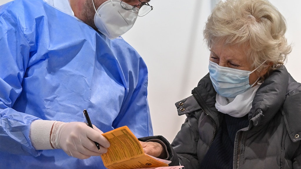 Die 81-jährige Gisela Rojek schaut im Impfzentrum Cottbus zusammen mit dem Arzt Michael Sasse nach ihrer Corona-Impfung in ihrem Impfausweis.