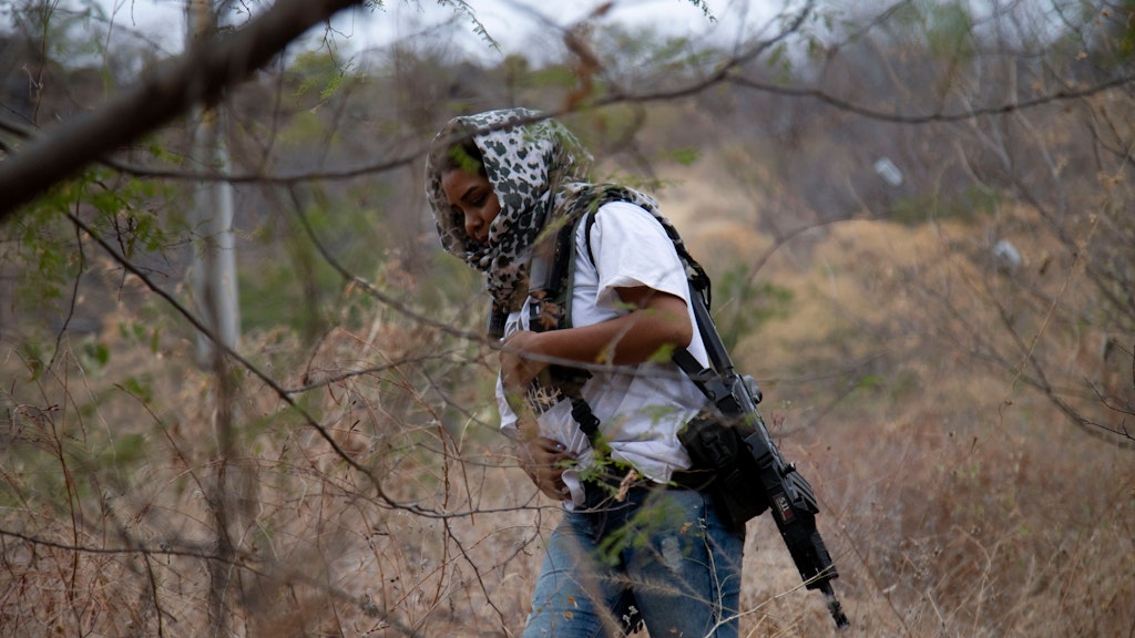 Eine Frau mit Sturmgewehr streift durchs Gelände. Sie gehört zu der Truppe, die von sich sagt, das Eindringen eines Drogenkartells in ihren mexikanischen Bundesstaat Michoacán verhindern zu wollen. 