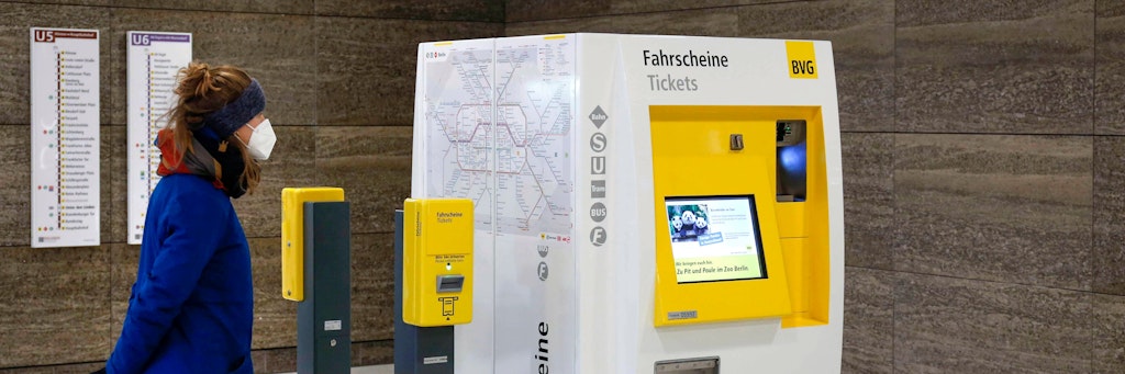 Eine Frau mit FFP2-Maske steht vor einem Automaten der BVG.