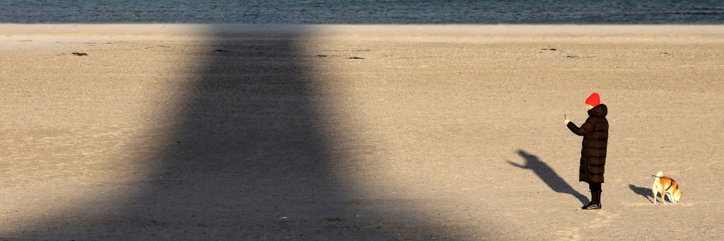 Eine Frau ist mit ihrem Hund in Warnemünde am Ostseestrand unterwegs. (Symbolbild)