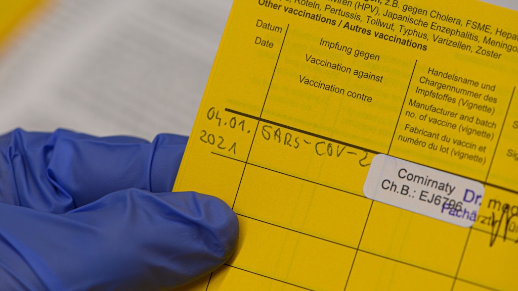 Eine Mitarbeiterin im Städtischen Klinikum Dresden hält einen Impfausweis mit der eingetragenen Impfung gegen Corona in den Händen. 
