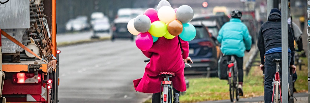 Eine junge Frau fährt mit bunten Luftballons auf ihrem Fahrrad durch Berlin.