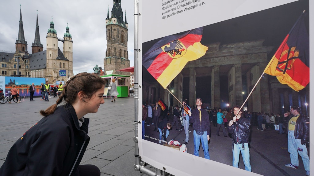 Eine junge Frau betrachtet auf dem Marktplatz in Halle (Saale) ein Foto von einem früheren „Tag der Deutschen Einheit“.