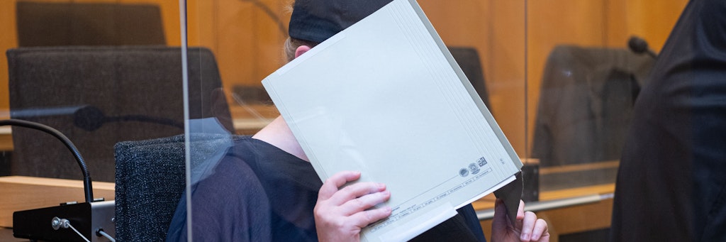 Zu Beginn des Prozesses im Missbrauchskomplex Münster sitzt die Mutter eines Opfers im Landgericht Münster und verdeckt ihr Gesicht mit einer Mappe. Die Anklage wirft der 31-Jährigen vor, den schweren sexuellen Missbrauch ihres heute elfjährigen Sohnes durch ihren Lebensgefährten nicht verhindert zu haben, obwohl sie davon wusste. 