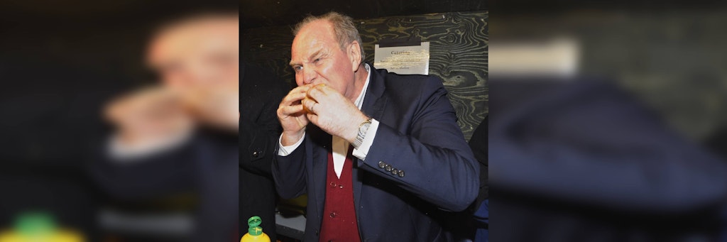 Herzhaft beißt Uli Hoeneß in ein Brötchen mit Nürnberger Bratwürsten