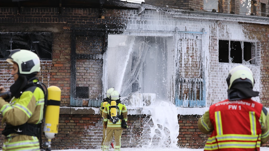 Feuerwehrmänner schießen Schaum in das Gebäude, um Flammen zu ersticken.