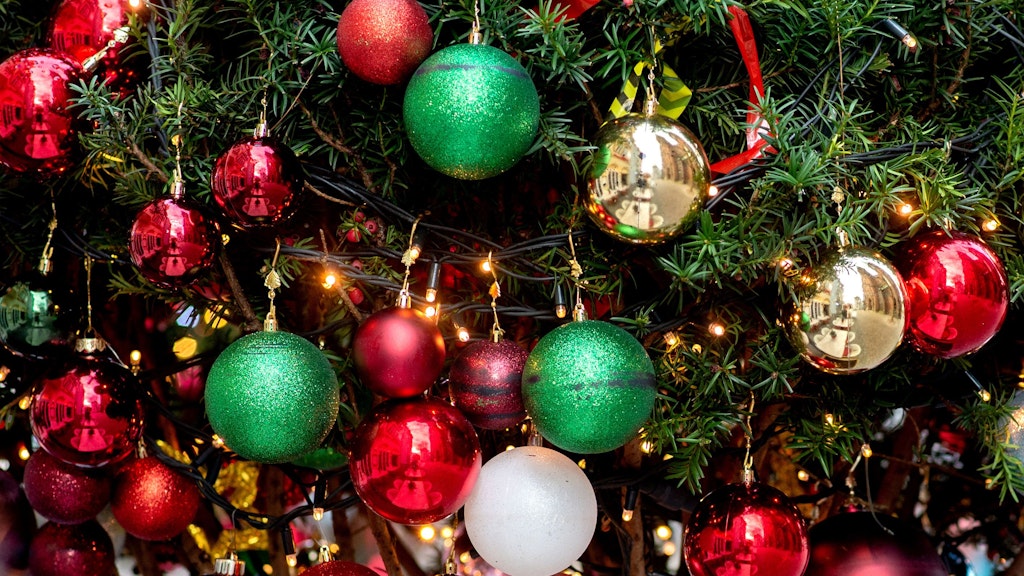 Ein Weihnachtsbaum ist mit zahlreichen Christbaumkugeln und Lichterketten weihnachtlich geschmückt. 