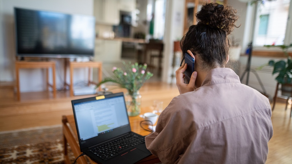 Eine Frau nimmt im Homeoffice aus ihrem Wohnzimmer an einer Telefonkonferenz teil. 