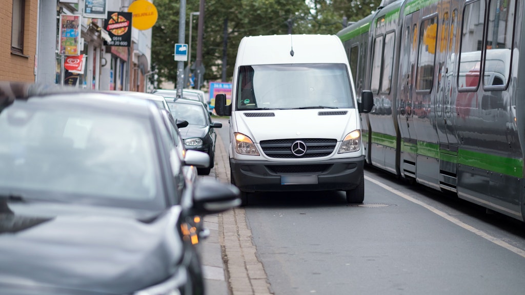 Ein Lieferwagen steht auf einer Straße neben parkenden Autos, daneben steht eine Straßenbahn entlang. Solche Verkehrsverstöße werden künftig deutlich teurer.