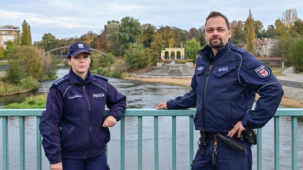 Die Polizisten Julita Cholewińska und Holger Welkisch auf der Stadtbrücke über die Neiße. Im Hintergrund die Reste des Ende 1945 abgebrannten Gubener Theaters. 