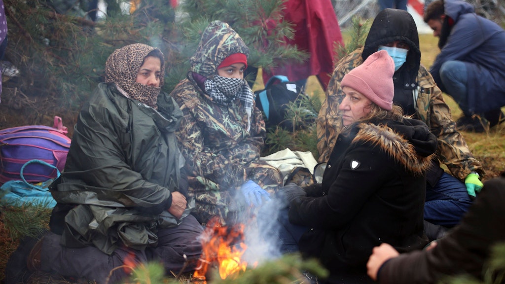 Frauen wärmen sich vor der polnischen Grenze an einem Feuer. Migranten haben sich in der Nähe der weißrussisch-polnischen Grenze versammelt und ruhen sich an einem Feuer aus. Mehrere Hundert Migranten haben sich nach Angaben der Behörden in Belarus zu Fuß auf den Weg zur Grenze zum EU-Nachbarland Polen gemacht. Foto: /BelTA/AP/dpa +++ dpa-Bildfunk +++