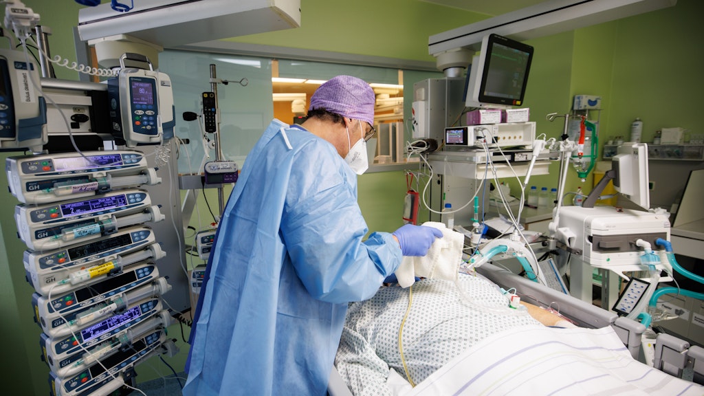 Ein Intensivmediziner arbeitet in Schutzkleidung in einem Intensivbett-Zimmer am Bett eines über einen Luftröhrenschnitt beatmeten Corona-Patienten. F