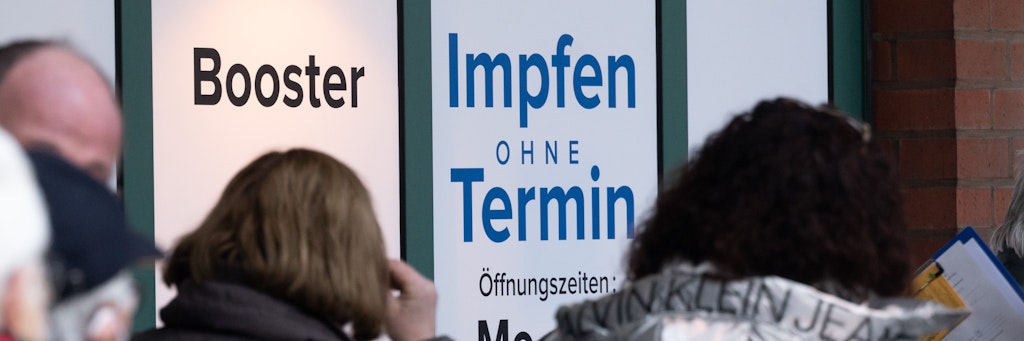Menschen stehen in einer Schlange und warten vor einem Impfzentrum.