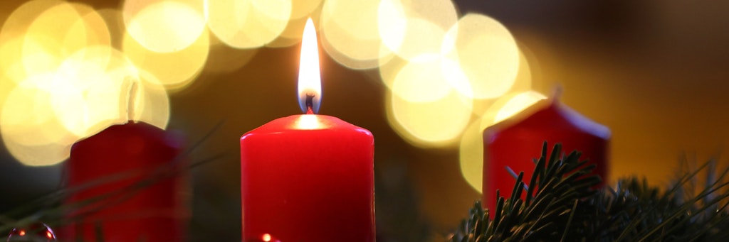 Eine Kerze brennt an einem Adventskranz.