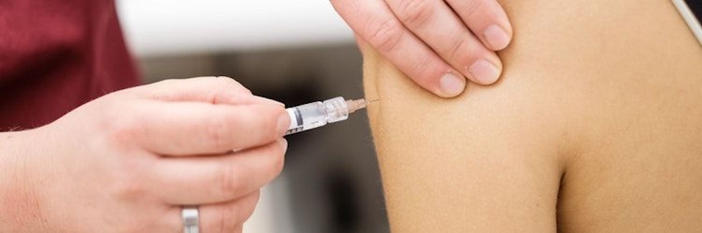 Eine Arzthelferin impft eine junge Patientin mit einer Spritze. 