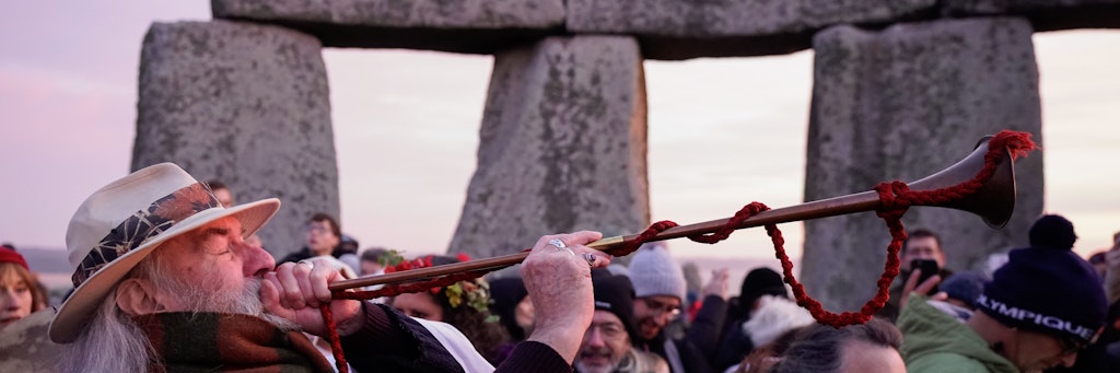 Ein Mann bläst ein Horn, während sich einige Menschen versammeln, um am prähistorischen Monument von Stonehenge auf der Salisbury Plain an den Feierlichkeiten zur Wintersonnenwende teilzunehmen.