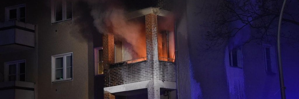 Die Wohnung steht in Flammen, Rauch dringt über den Balkon nach draußen.