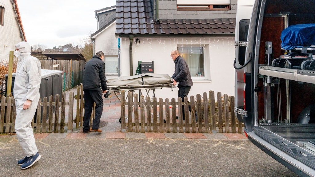 Zwei Bestatter bringen eine Trage mit einem Leichnam aus einem Haus in Glinde.